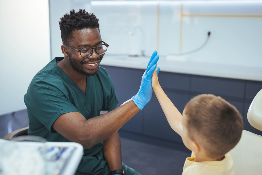 Dental assistant high fiving pediatrics patient after successful teeth cleaning