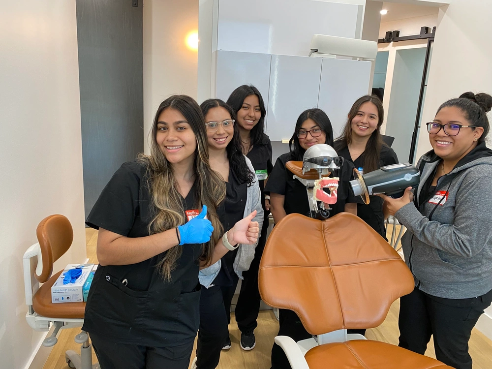 aspiring dental assistants posing in examination room with handheld x-ray system